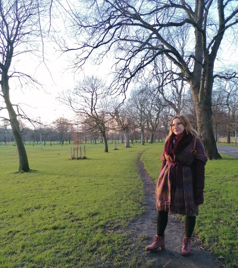 Image of a smiling Zsofia Kaplar, sitting on a wicker chair with a notebook next to plants